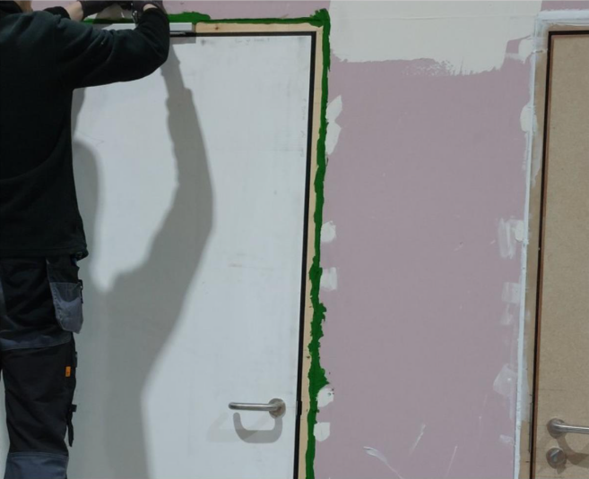 A man is putting a fire door product around the fire door to check how it performs.